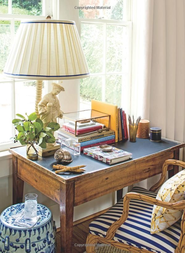 a lamp sitting on top of a wooden table next to a chair and ottoman in front of a window