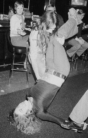 black and white photograph of people sitting at tables with one person falling on the floor