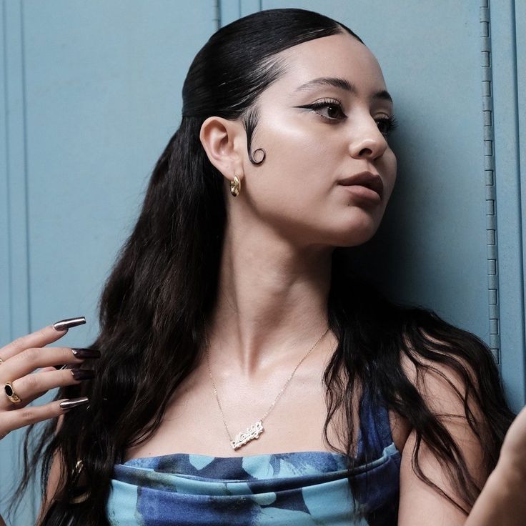 a woman leaning against a blue wall with her hand on her hip and looking off to the side