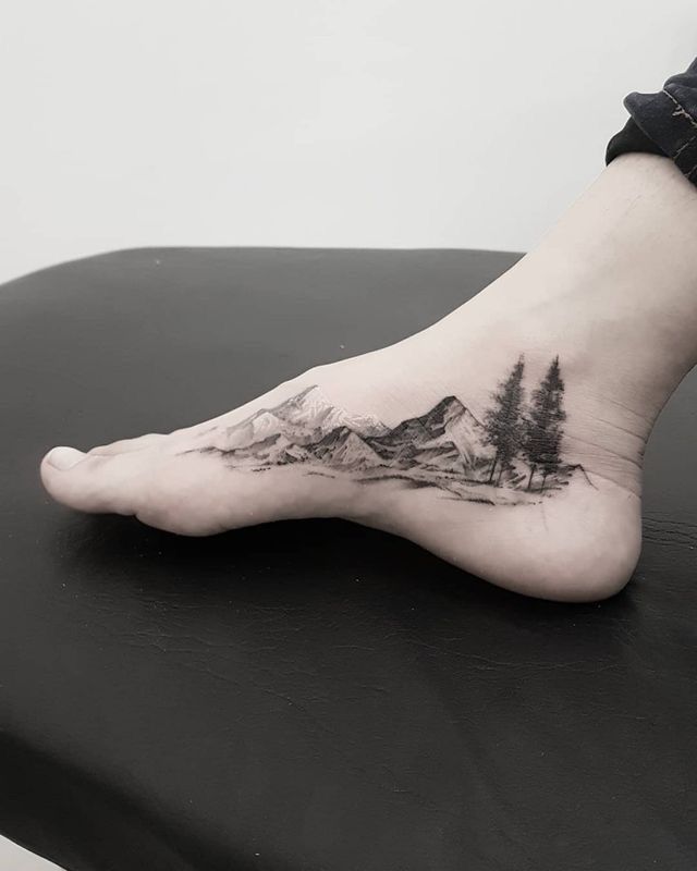 a person's foot with mountains and trees on it