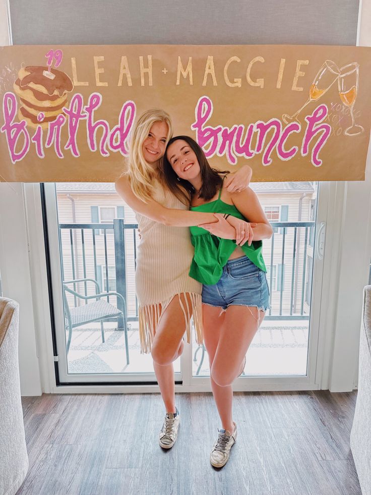 two women standing in front of a birthday banner and holding each other's arms