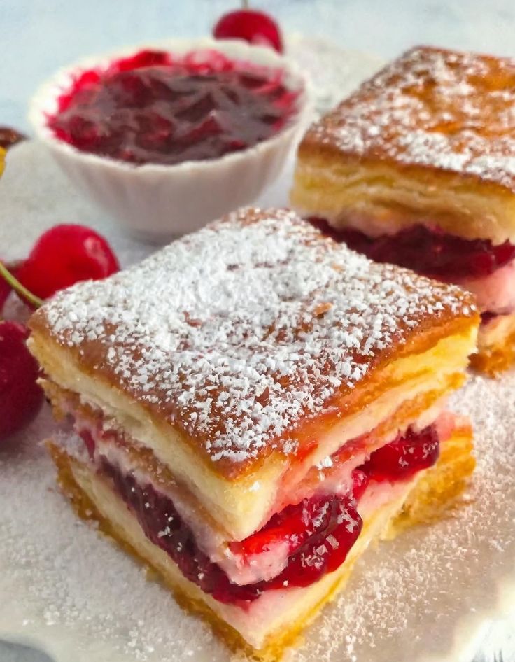 two desserts on a plate with cherries and powdered sugar next to them