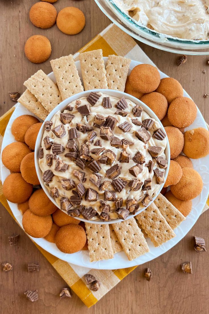 two plates filled with crackers and cheesecake dip on top of each other next to cookies