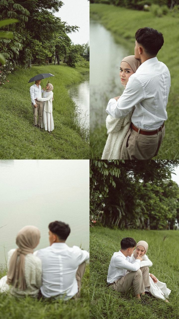 two people sitting on the grass next to a body of water and one person holding an umbrella