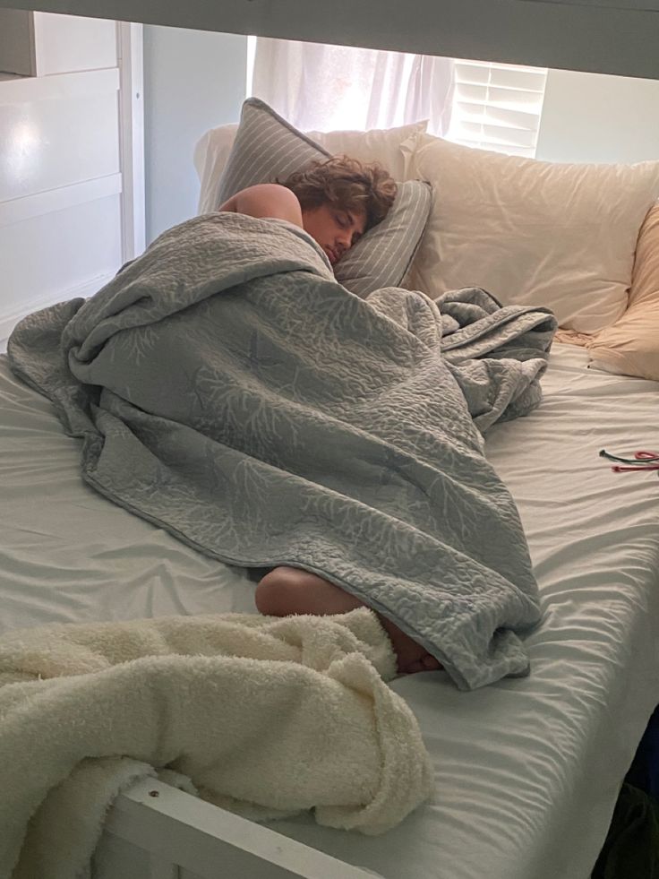 a person laying on a bed with a blanket over their head and the sheets are pulled back