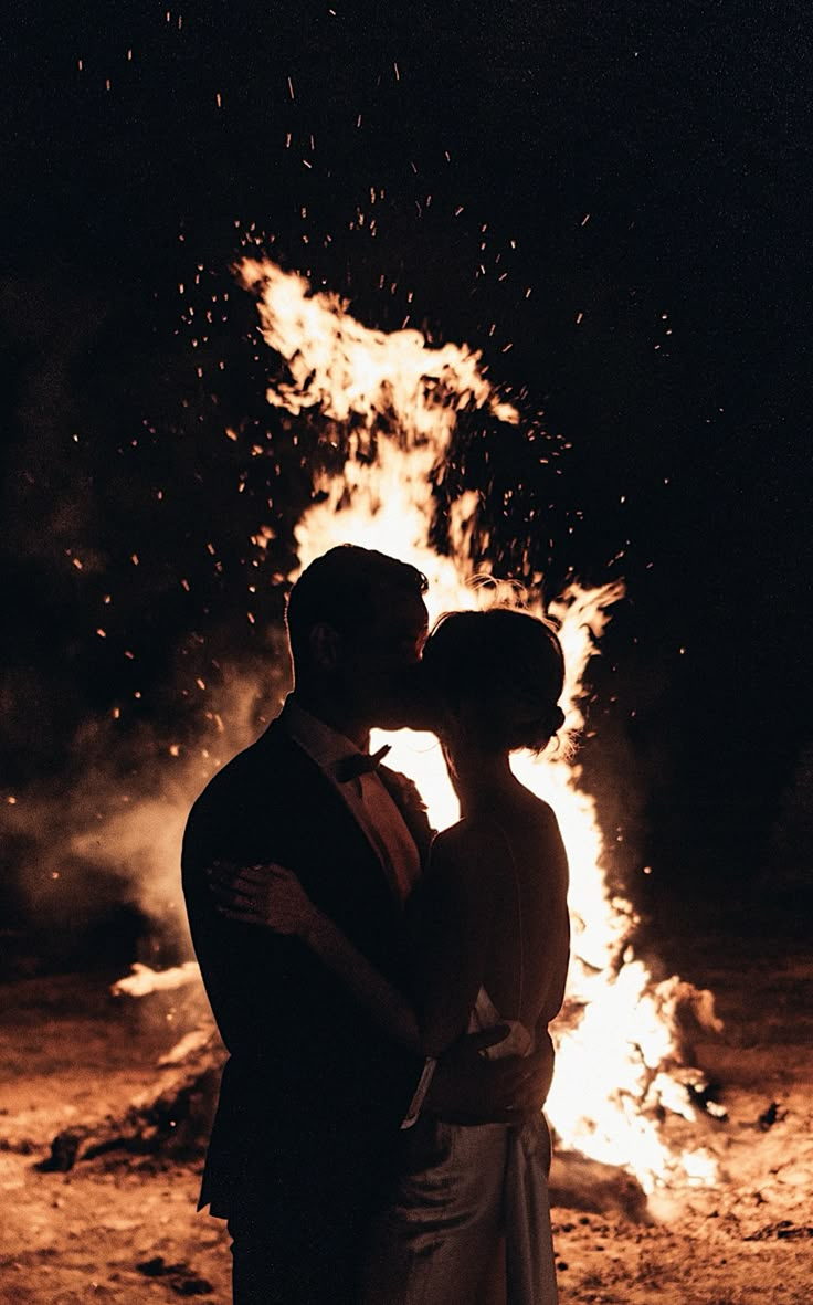 a bride and groom standing in front of a fire