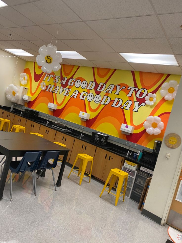 an empty cafeteria with tables and yellow stools in front of a large sign on the wall