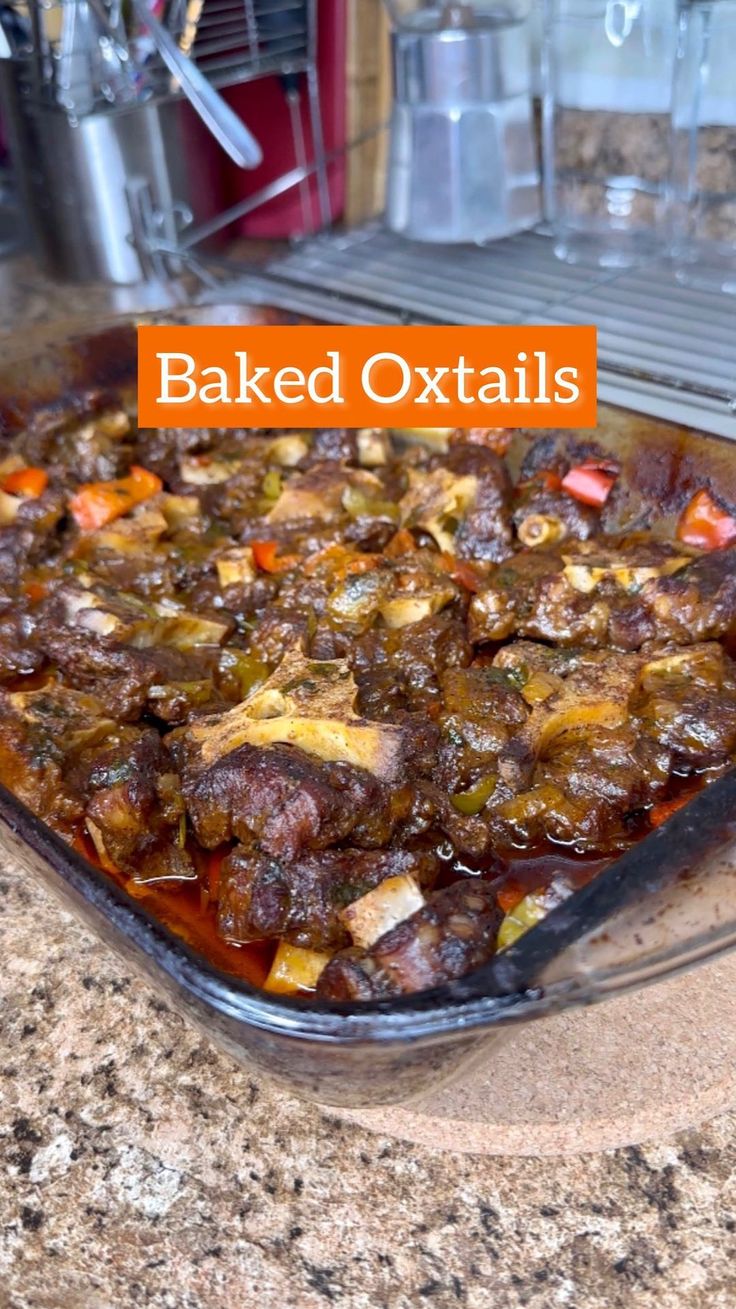 baked oxtails in a glass dish on a granite countertop with the words baked oxtails above it