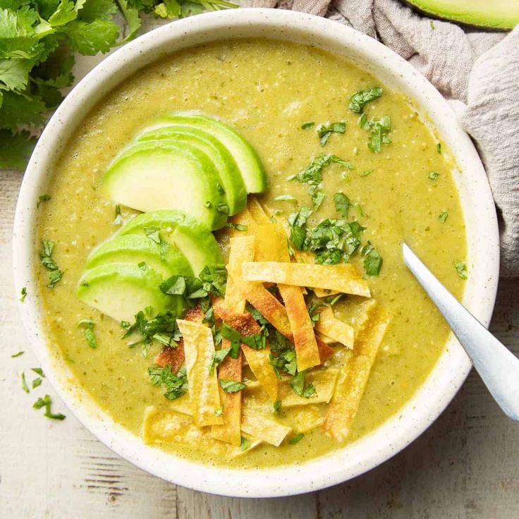 a white bowl filled with soup topped with tortilla chips and avocado