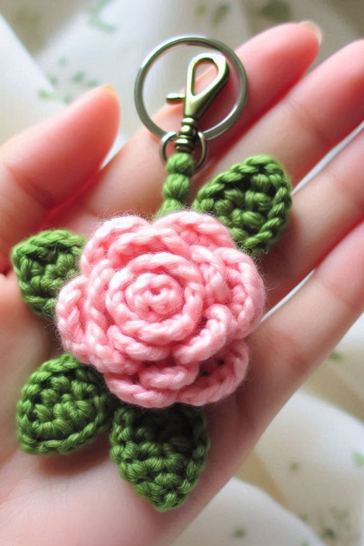 a hand holding a pink and green crocheted flower on a metal keychain