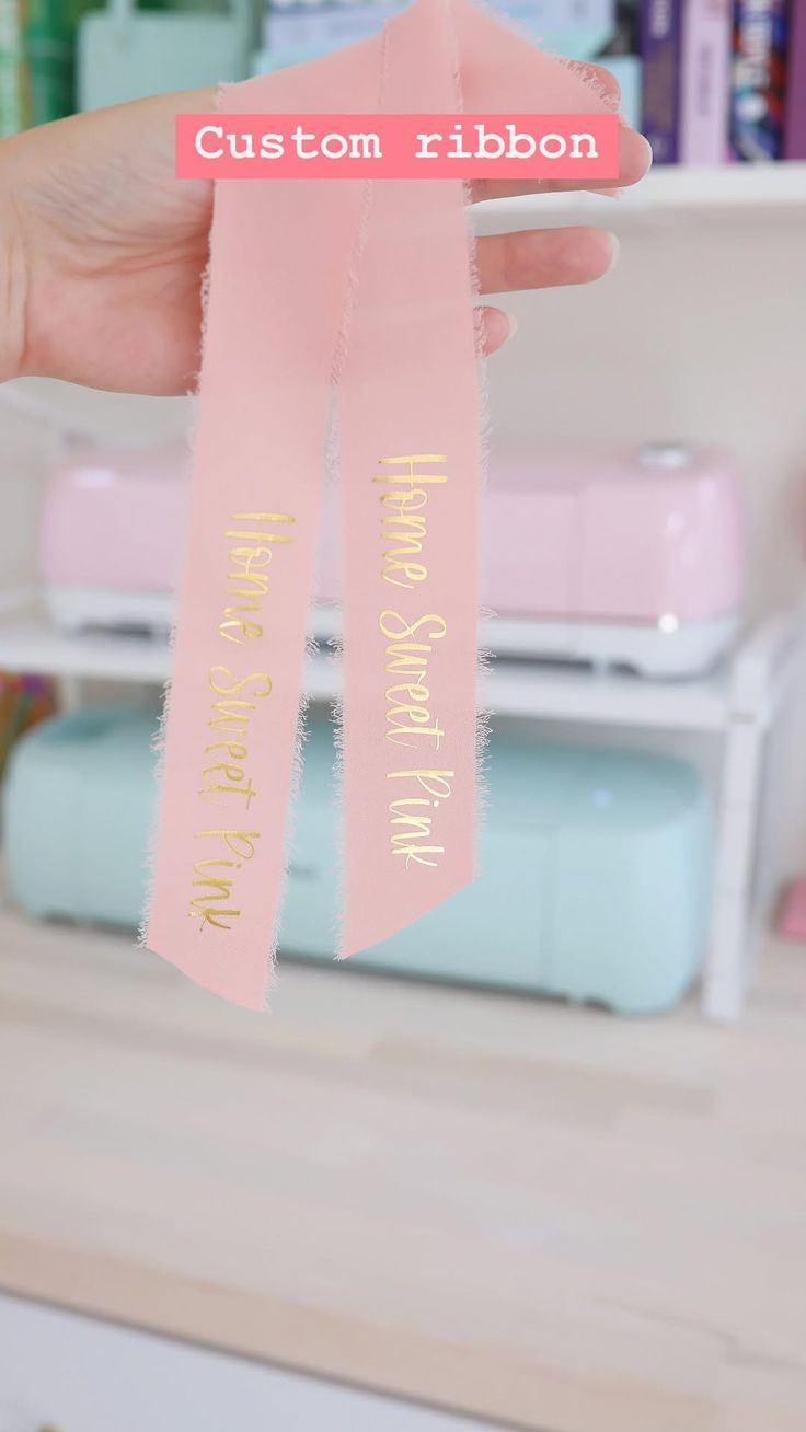 a person holding up a pink ribbon with the words custom ribbon written in gold on it