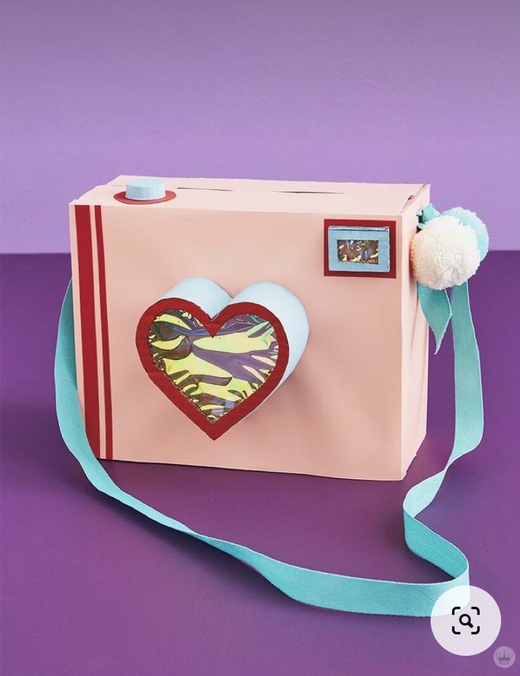 a pink box with a heart on it and a blue ribbon around the bottom that has a pom - pom attached