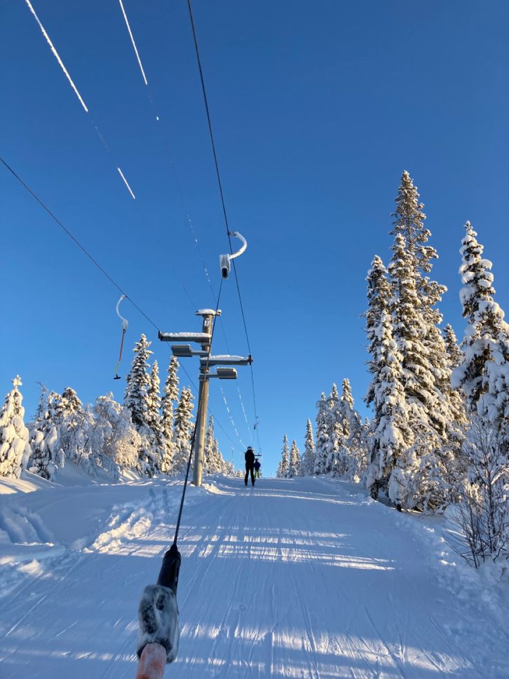 a person riding skis down a snow covered slope next to a ski lift and trees