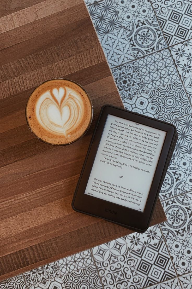 a tablet sitting next to a cup of coffee on top of a wooden table with a heart drawn in it