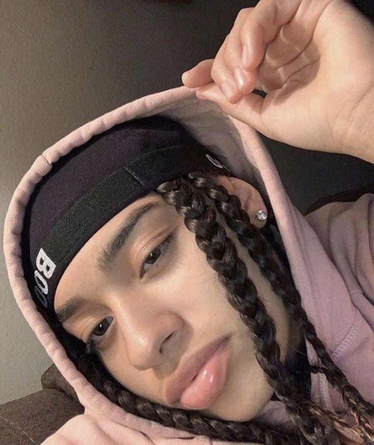 a woman with braids on her head wearing a pink hoodie and looking at the camera