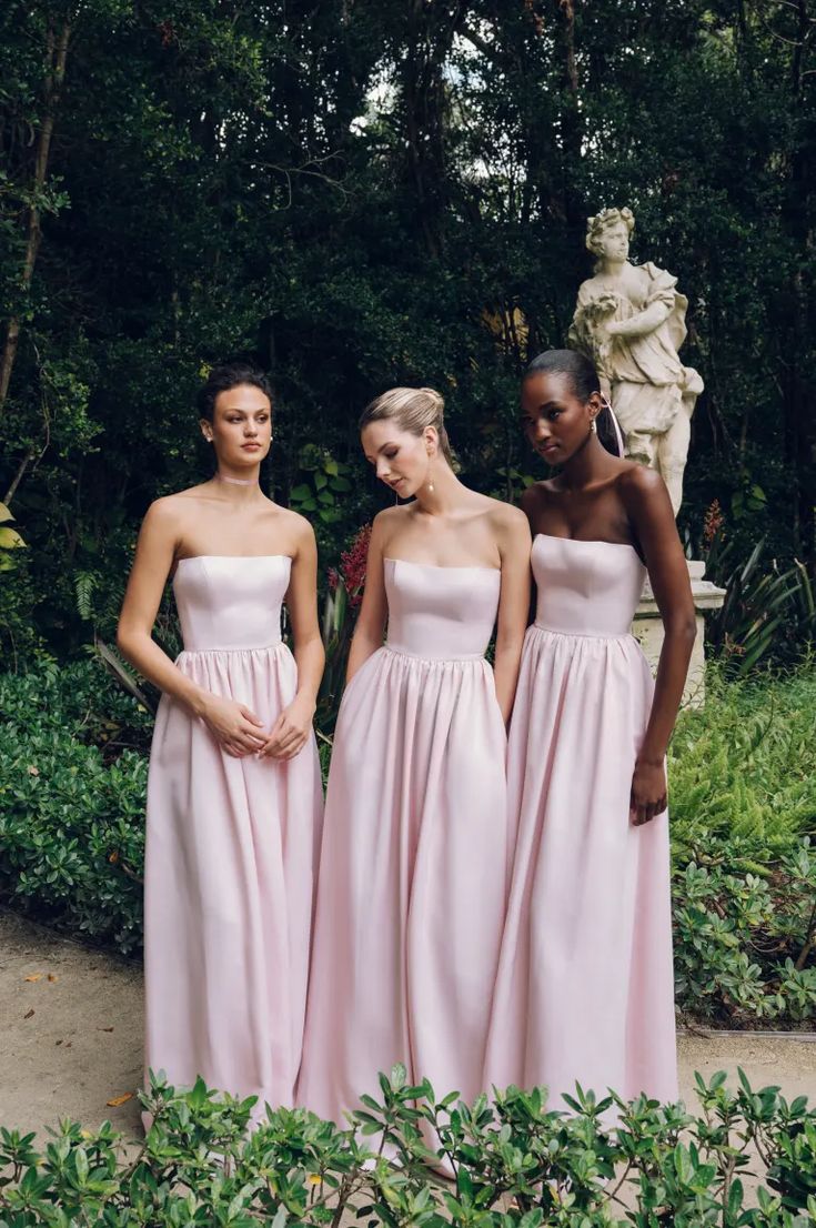 three women in long pink dresses standing next to each other near some bushes and trees