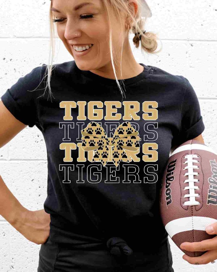 a woman holding a football and wearing a t - shirt with the words tigers on it