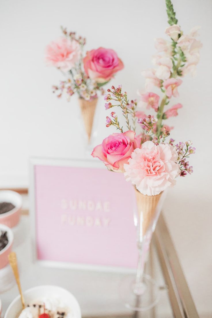 some pink flowers are in a vase on a table next to other desserts and drinks