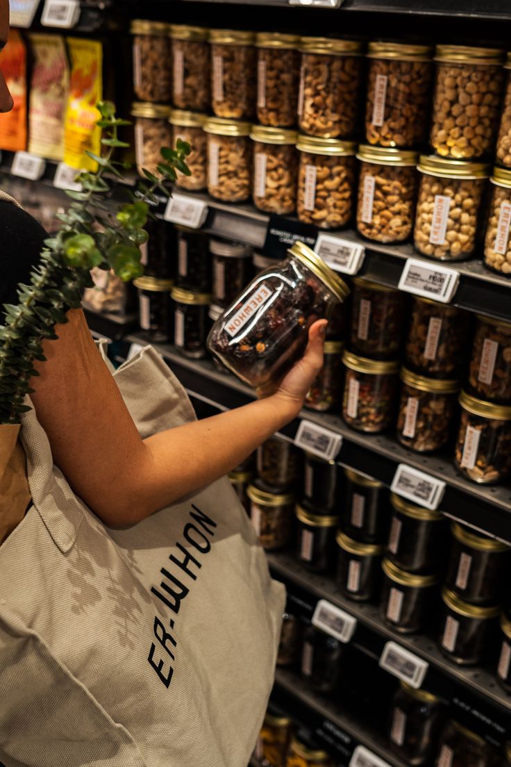 a woman holding a jar filled with food in front of shelves full of nuts and other items