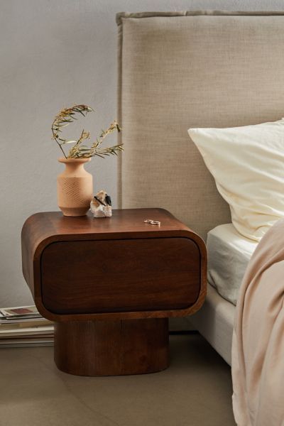 a bed with a wooden night stand next to it and a vase on the nightstand