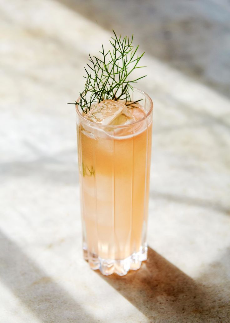 a tall glass filled with a drink and garnished with a sprig of rosemary