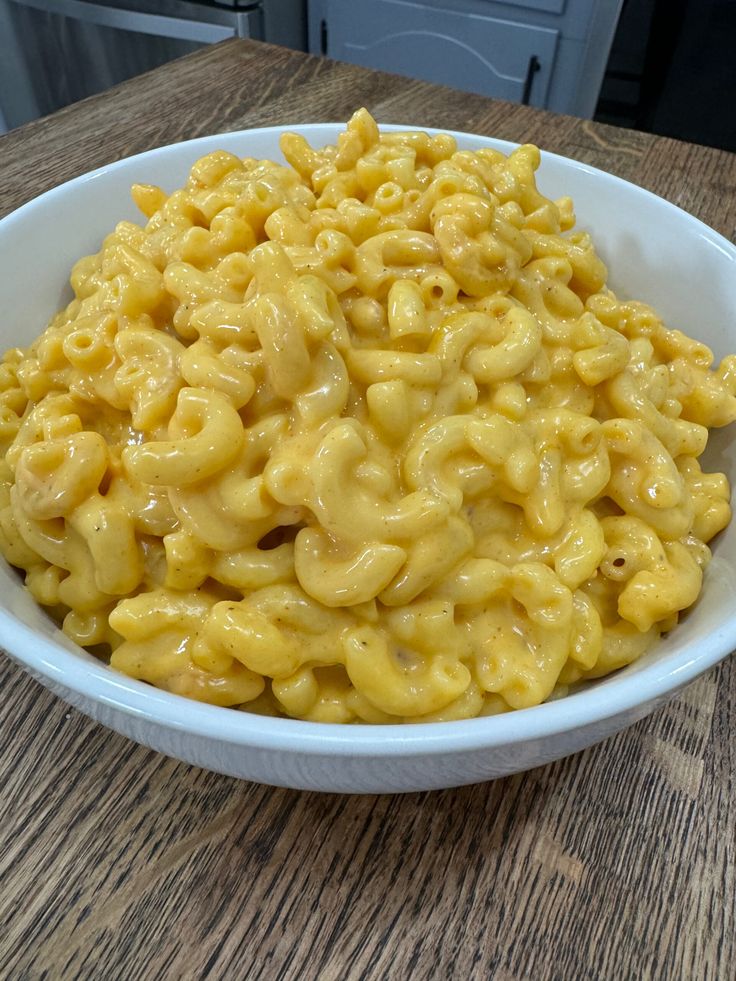 a white bowl filled with macaroni and cheese on top of a wooden table