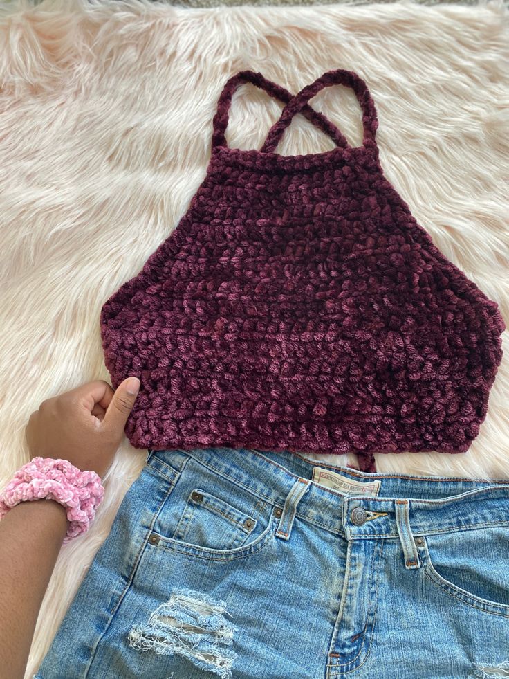 a woman's hand is holding onto a crocheted crop top and denim shorts