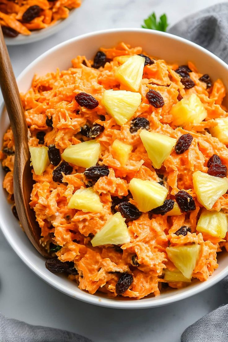 a white bowl filled with carrot salad next to a wooden spoon