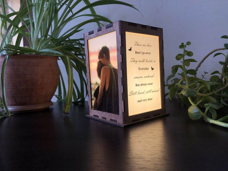 an illuminated photo frame sitting on top of a wooden table next to potted plants