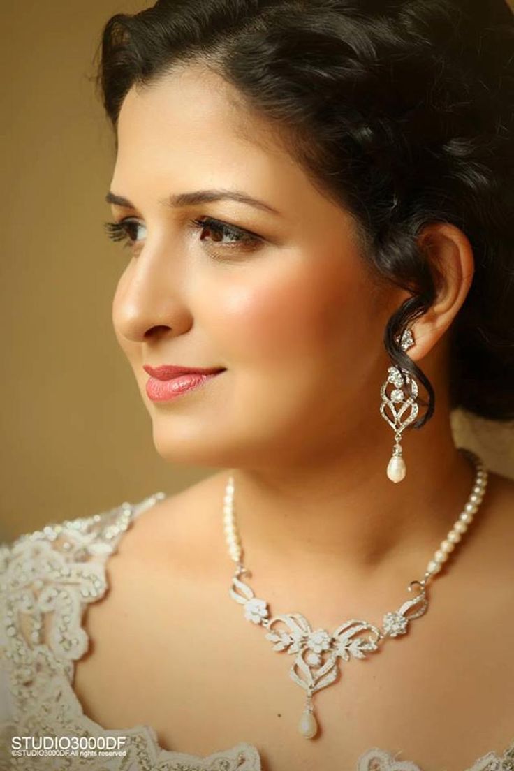 a woman in a wedding dress wearing pearls and earrings on her head, looking off to the side