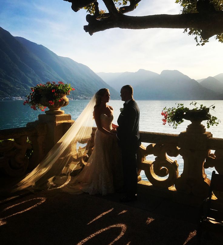 a bride and groom standing next to each other in front of a lake at sunset