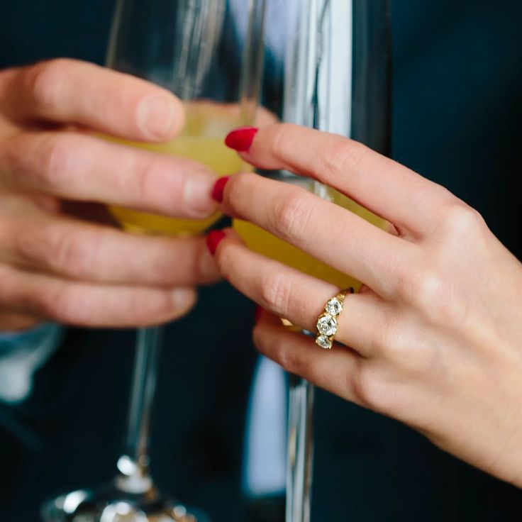 two people are holding wine glasses with their hands on the glass and one is wearing a diamond ring