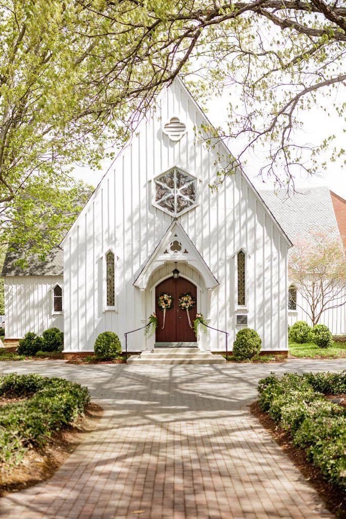 a white church with a red door surrounded by greenery