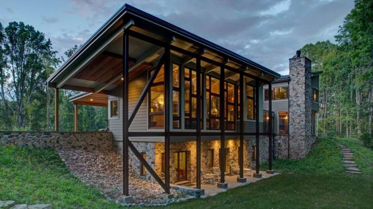 a modern house in the woods with stone walls and glass windows on the front porch