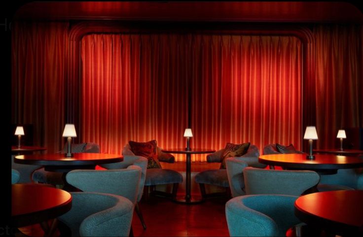 an empty restaurant with blue chairs and red curtains on the wall behind it is a round dining table