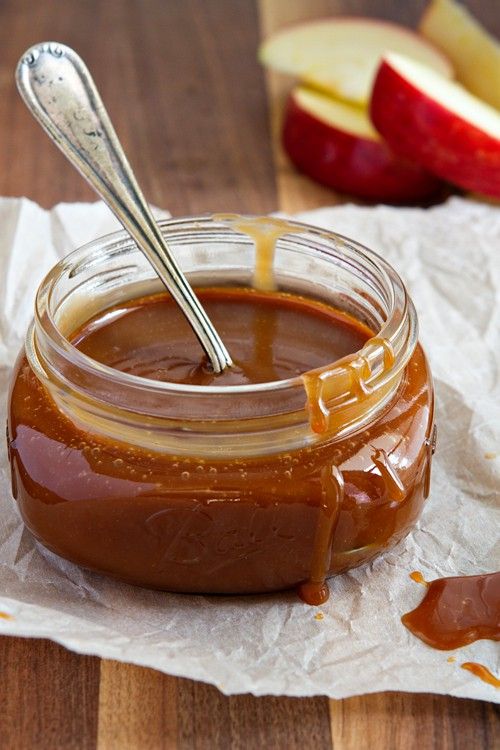 a spoon in a jar filled with caramel sauce next to sliced apples and paper towels