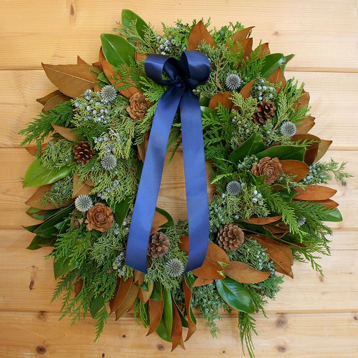 a wreath with pine cones, evergreens and blue ribbon on a wooden table top