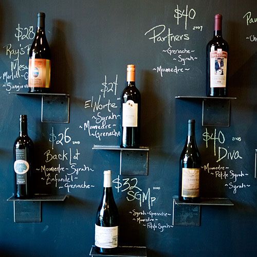 several bottles of wine are lined up on the wall in front of a chalkboard