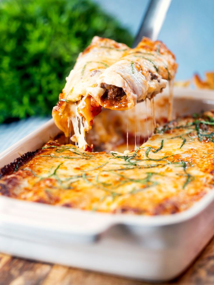 a piece of lasagna being lifted from a casserole dish with cheese and herbs