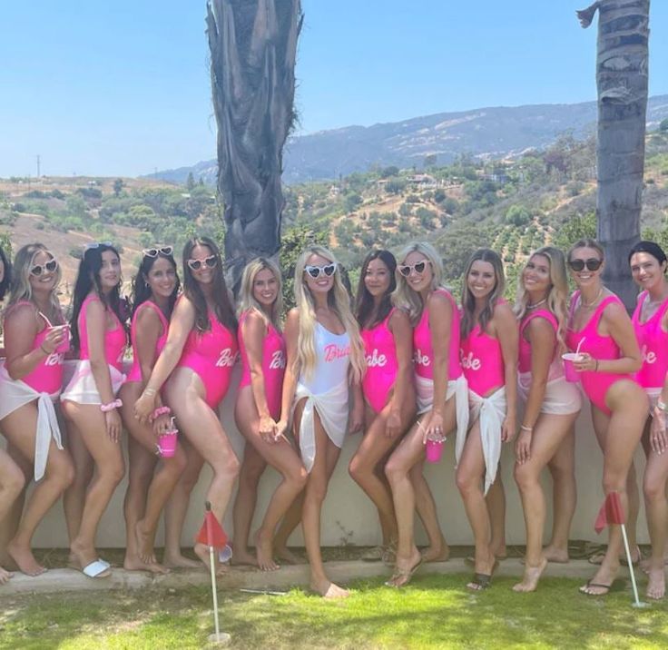 a group of women in pink bathing suits posing for a photo with palm trees behind them