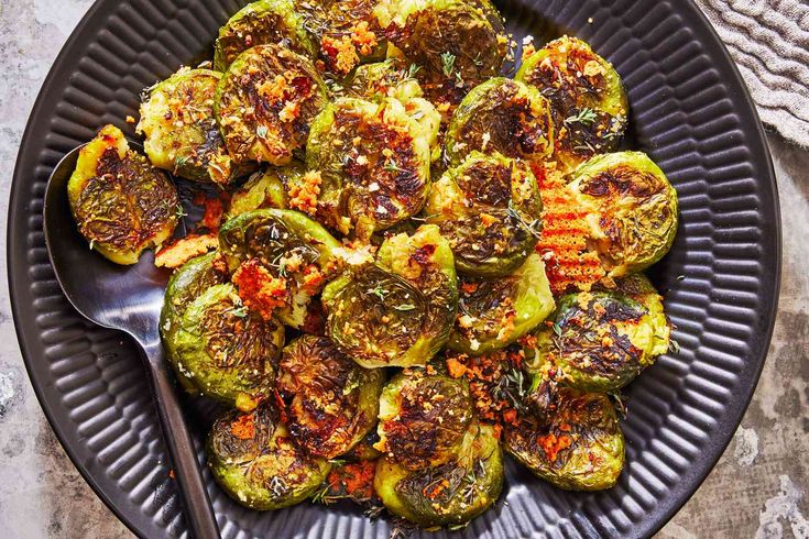 cooked brussel sprouts on a black plate with a spoon and napkin