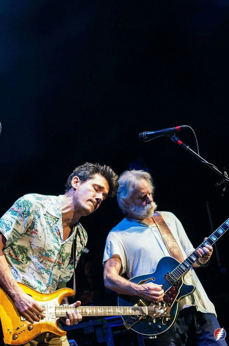 two men standing next to each other while playing guitars