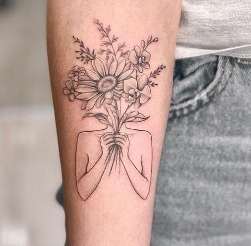 a woman's arm with a tattoo on it and flowers in the vase behind her