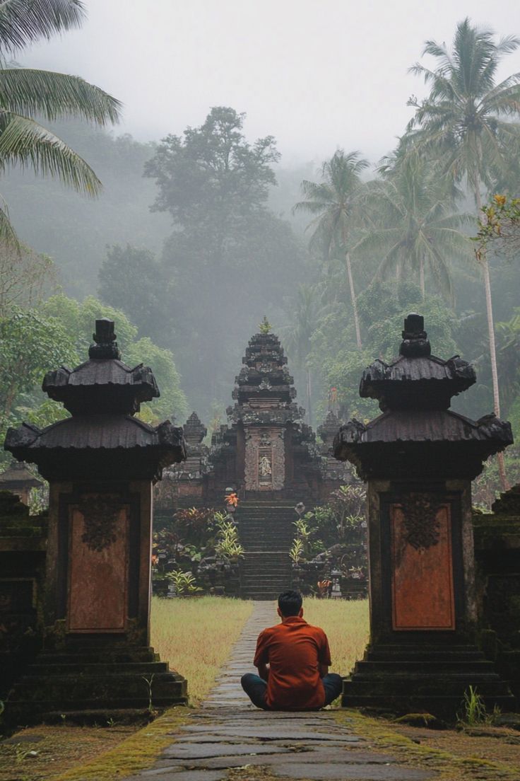 a person sitting on the ground in front of some stone pillars with trees and bushes behind them