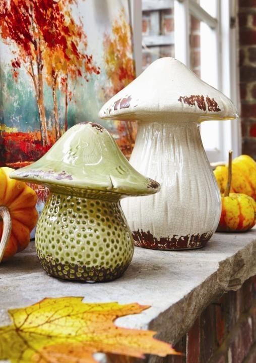 three ceramic mushrooms sitting on top of a table next to autumn leaves and pumpkins