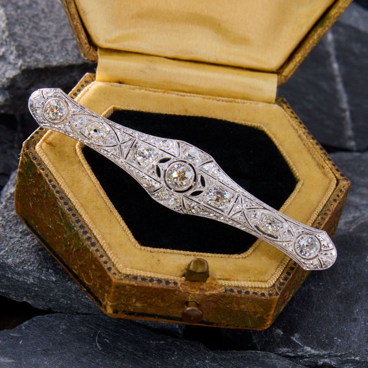 This fabulous circa 1920s platinum brooch is finished with an 18k white gold locking pin stem. The brooch features a pierced design with milgrain edging. The brooch is accented with three (3) bezel set old European cut diamonds and six (6) prong set old mine cut diamonds. The brooch measures 66.4mm X 12.7mm. Vintage Platinum Brooches With Diamond Accents, Antique White Gold Brooches With Diamond Accents, Vintage Platinum Brooches For Wedding, Art Deco White Gold Brooch In Platinum, Art Deco Platinum Brooches In White Gold, Art Deco White Gold Platinum Brooches, Victorian White Gold Brooches With Diamond Accents, Vintage White Gold Brooches With Diamond Accents, Classic Platinum Brooches With Diamond Accents