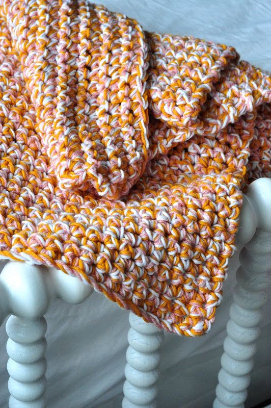 an orange and white crocheted blanket sitting on top of a bed