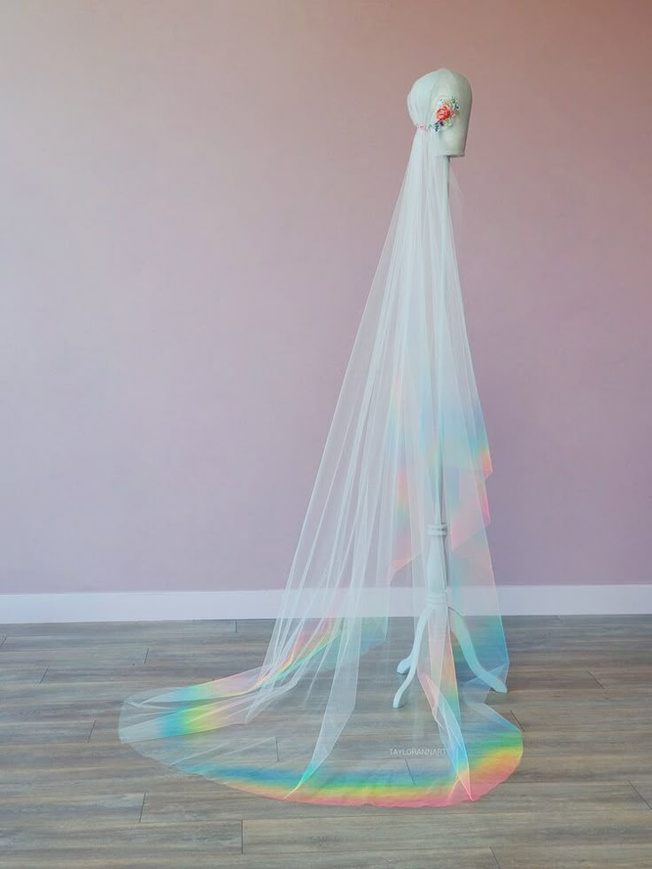 a white veil hanging from the side of a mannequin's head in front of a pink wall