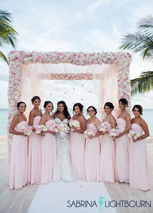 a group of women standing next to each other in front of a white and pink wedding arch