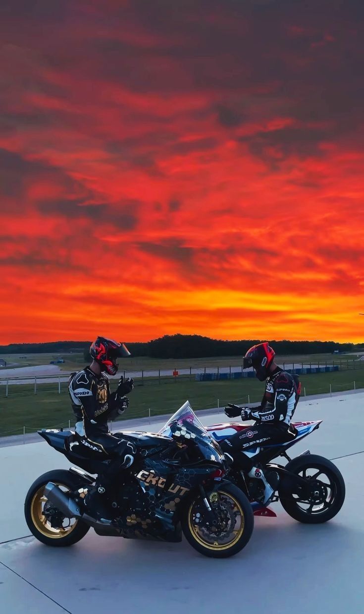 two motorcyclists are sitting on their bikes in front of a colorful sunset